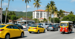 Cars, tuk tuks, and taxis on sunny tropical road, palm trees nearby.