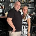 Two people smiling in front of a bar.