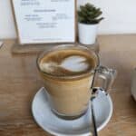 Cappuccino on wooden table, menu in background.