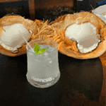 Coconut drink with mint garnish on dark table.