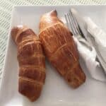 Two croissants on a plate with cutlery.