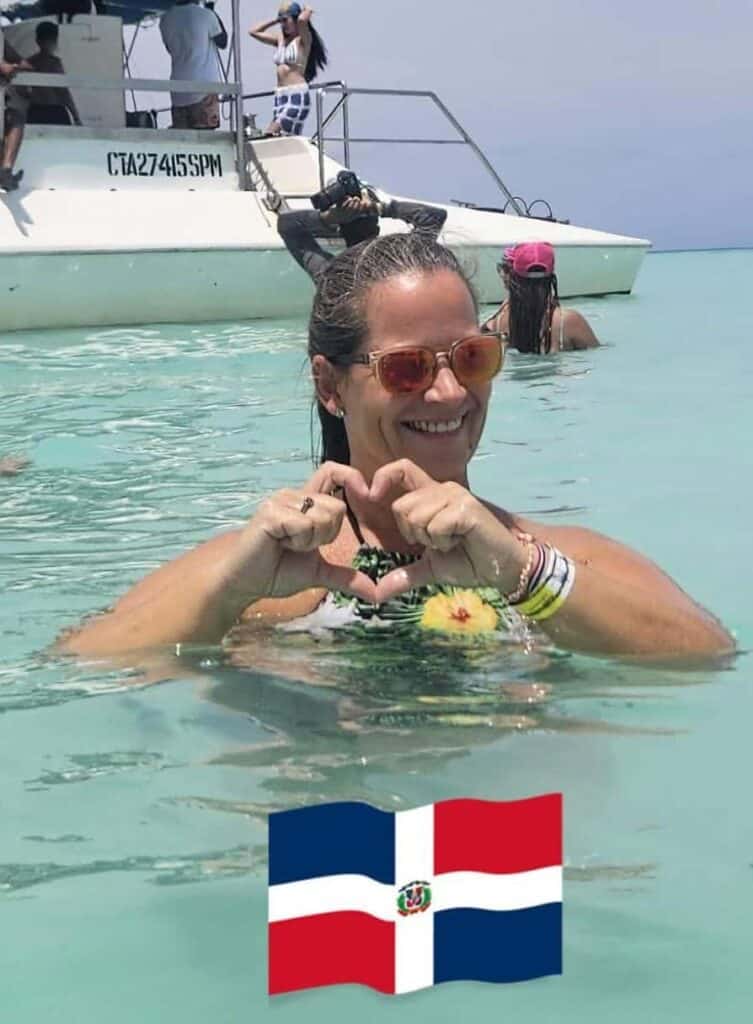 Smiling woman in water near boat, heart gesture.