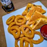 Onion rings, quesadillas, ketchup, and beer on table.