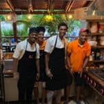Chefs smiling in kitchen with fresh pineapples.