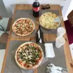 Three pizzas and Coke on wooden table.