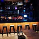 Modern bar interior with stools and illuminated shelves.