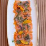Salmon carpaccio with herbs and orange slices