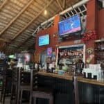 Tropical bar with drinks, TV, and high stools.
