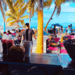 Beach bar scene with people and palm trees.