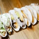 Assorted tacos with various fillings on wooden table.