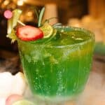 Green cocktail with strawberry and lime garnish.