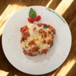 Cheesy pizza on a white plate with herbs.