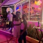 Two friends outside a neon-lit café at night.