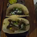 Two tacos with beef and toppings on wood table.