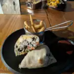 Burrito with fries and sauce on black plate.