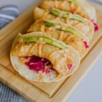 Tacos with avocado and sauce on wooden board.