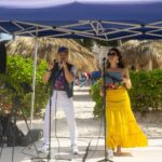 Singers performing under a blue canopy at the beach.