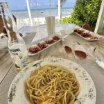 Seaside dining with spaghetti and drinks.