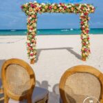 Beach wedding arch with flowers and chairs.