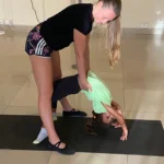 Instructor helping child in yoga pose on mat